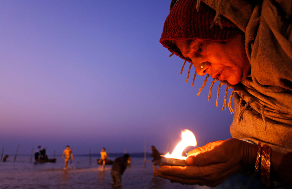 2012年1月14日，印度的阿拉哈巴德马尔卡 Sankranti 节上，一个印度教的信徒在恒河，亚穆纳河和萨拉斯瓦蒂河的汇流处手举着一盏油灯对着太阳神在祈祷。在庆祝Magh Mela节的45天黄道吉日活动中，成千上万的印度教徒们在交汇处洗澡洗清自身的罪孽从而获得财富。（美联社/ Rajesh Kumar Singh）